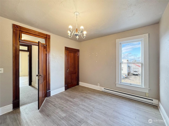 empty room featuring a baseboard heating unit, a textured ceiling, and a chandelier