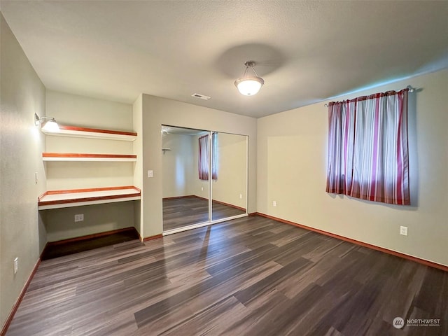 unfurnished bedroom with built in desk, a closet, and dark hardwood / wood-style floors