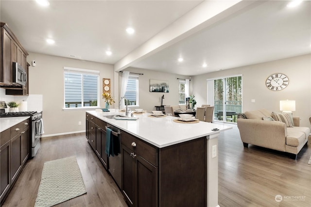 kitchen with stainless steel appliances, sink, light hardwood / wood-style flooring, a kitchen island with sink, and beam ceiling