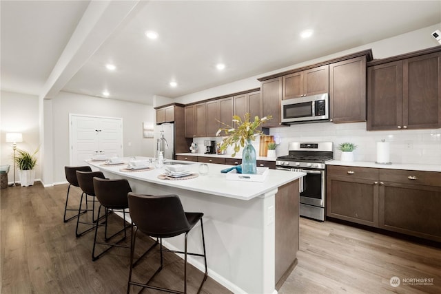 kitchen with a kitchen island with sink, a breakfast bar area, stainless steel appliances, sink, and light hardwood / wood-style flooring