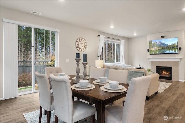 dining room featuring hardwood / wood-style flooring, a tiled fireplace, and a wealth of natural light