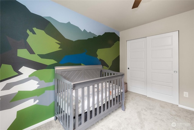 carpeted bedroom featuring a nursery area, ceiling fan, and a closet