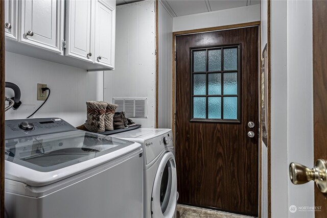 clothes washing area with cabinets, washing machine and dryer, and wooden walls