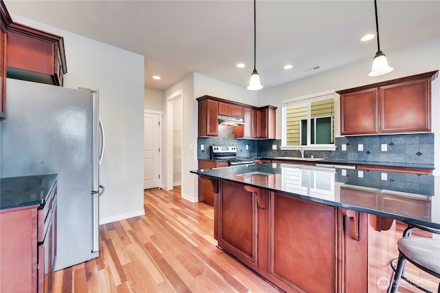 kitchen with appliances with stainless steel finishes, light hardwood / wood-style flooring, a breakfast bar area, and decorative light fixtures