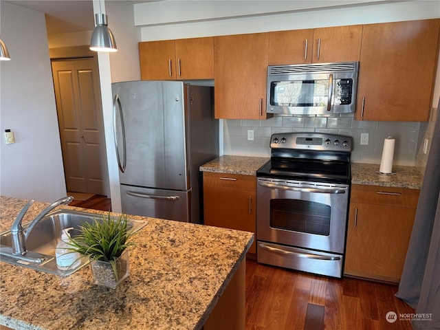 kitchen featuring stainless steel appliances, dark wood-type flooring, light stone counters, sink, and backsplash