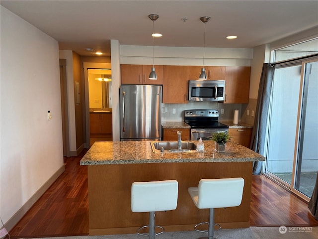 kitchen with appliances with stainless steel finishes, pendant lighting, a kitchen bar, decorative backsplash, and sink