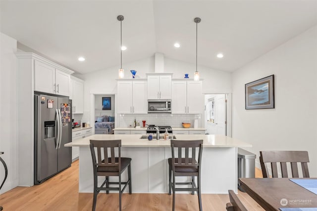 kitchen with decorative light fixtures, vaulted ceiling, white cabinets, and appliances with stainless steel finishes