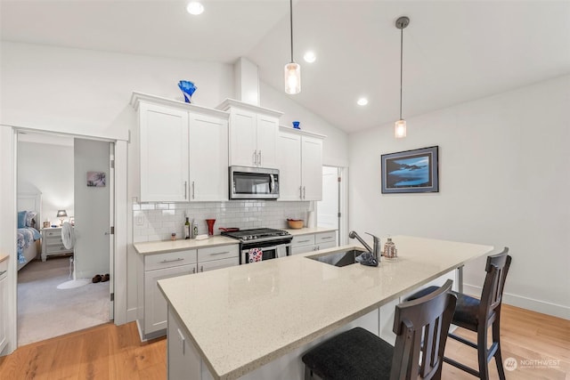 kitchen with vaulted ceiling, appliances with stainless steel finishes, pendant lighting, white cabinets, and sink