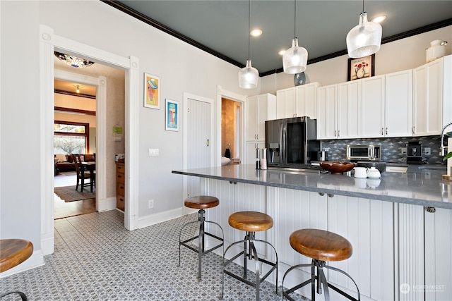 kitchen featuring backsplash, white cabinets, stainless steel fridge with ice dispenser, ornamental molding, and a breakfast bar area