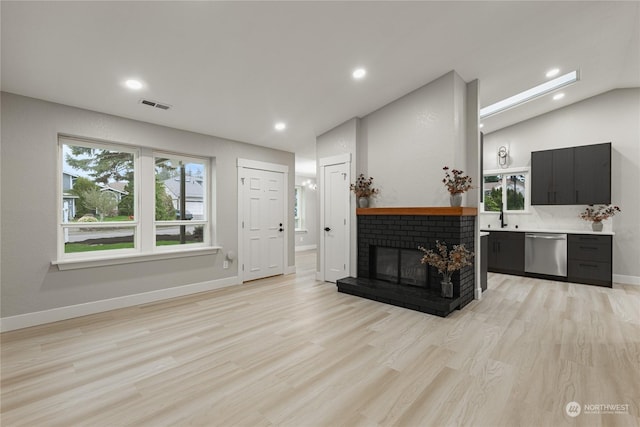 living room with sink, light hardwood / wood-style floors, a brick fireplace, and vaulted ceiling