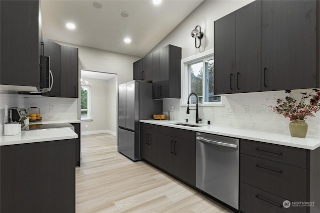 kitchen with appliances with stainless steel finishes, decorative backsplash, sink, light hardwood / wood-style flooring, and lofted ceiling