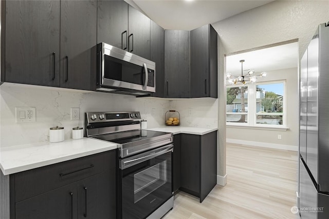 kitchen with stainless steel appliances, light hardwood / wood-style flooring, decorative backsplash, hanging light fixtures, and a chandelier