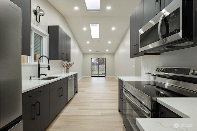 kitchen featuring vaulted ceiling, light hardwood / wood-style floors, stainless steel appliances, sink, and backsplash