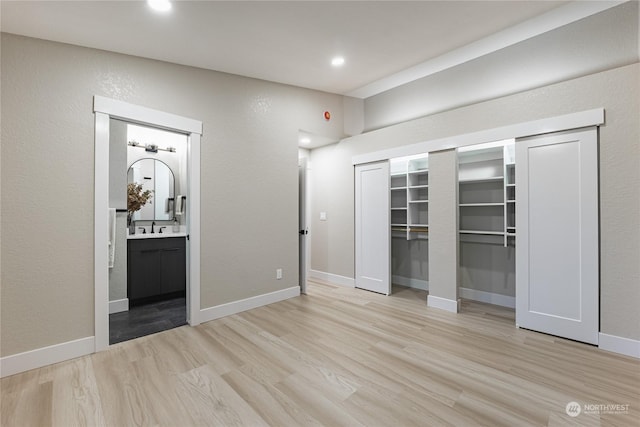 unfurnished bedroom featuring sink, light wood-type flooring, and ensuite bath