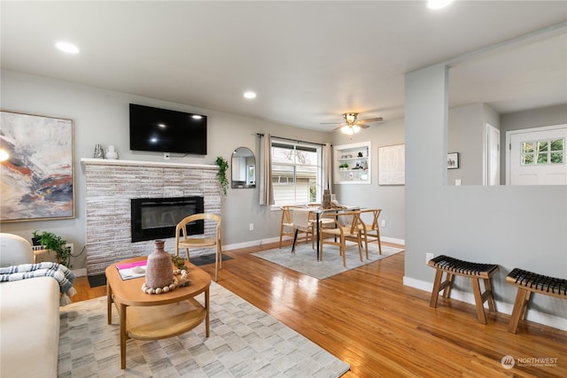 living room with built in shelves, light wood-type flooring, a fireplace, and ceiling fan