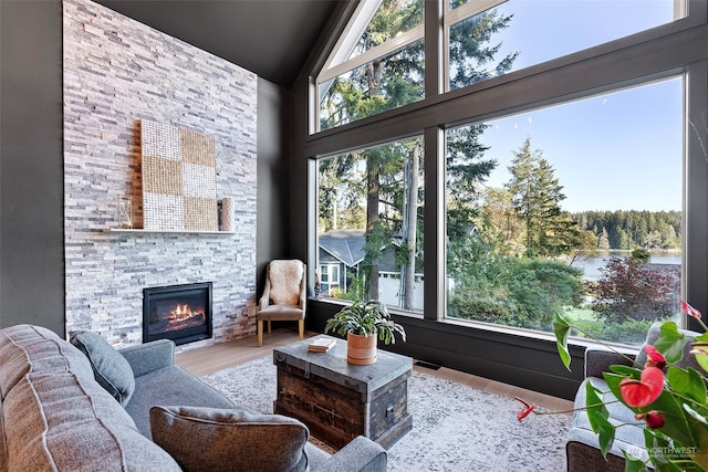 sunroom featuring lofted ceiling, a water view, and a stone fireplace