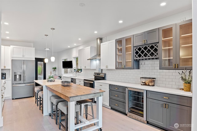 kitchen featuring appliances with stainless steel finishes, beverage cooler, gray cabinetry, and wall chimney exhaust hood