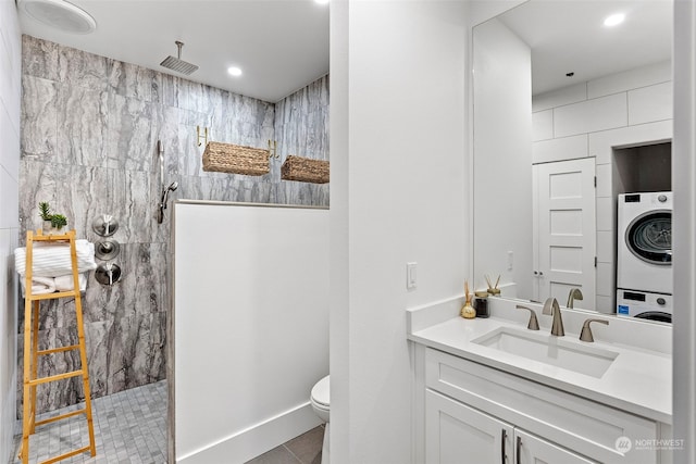 bathroom featuring toilet, vanity, tile patterned floors, stacked washer / dryer, and a tile shower