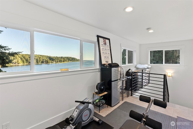 exercise area featuring a water view, light tile patterned floors, and a wealth of natural light