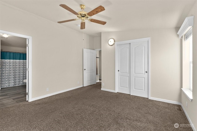 unfurnished bedroom featuring ensuite bath, dark colored carpet, a closet, vaulted ceiling, and ceiling fan