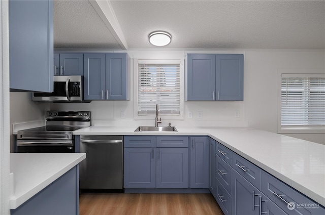 kitchen featuring sink, light wood-type flooring, appliances with stainless steel finishes, blue cabinetry, and a textured ceiling