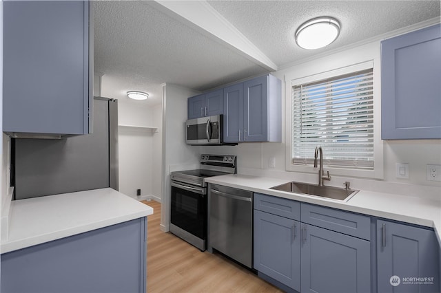 kitchen with sink, light hardwood / wood-style flooring, blue cabinetry, stainless steel appliances, and a textured ceiling