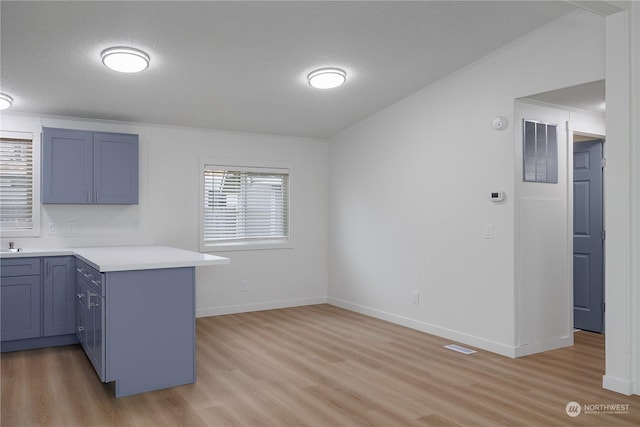 kitchen with light hardwood / wood-style floors, a textured ceiling, kitchen peninsula, and vaulted ceiling