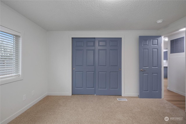 unfurnished bedroom with a textured ceiling, a closet, ornamental molding, and carpet floors