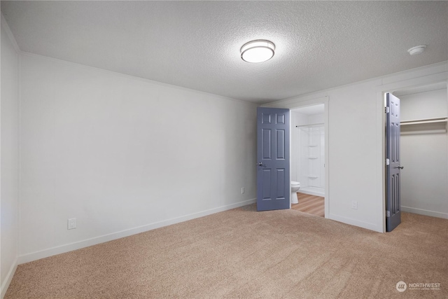 unfurnished bedroom with a textured ceiling, a closet, ensuite bathroom, and light colored carpet