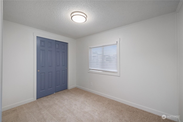 unfurnished bedroom featuring a textured ceiling, a closet, ornamental molding, and light colored carpet