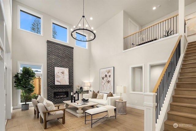 living room with light hardwood / wood-style floors, a brick fireplace, a towering ceiling, and a chandelier