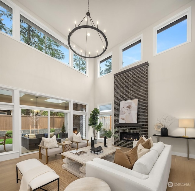 living room with a healthy amount of sunlight, light hardwood / wood-style floors, a towering ceiling, an inviting chandelier, and a fireplace