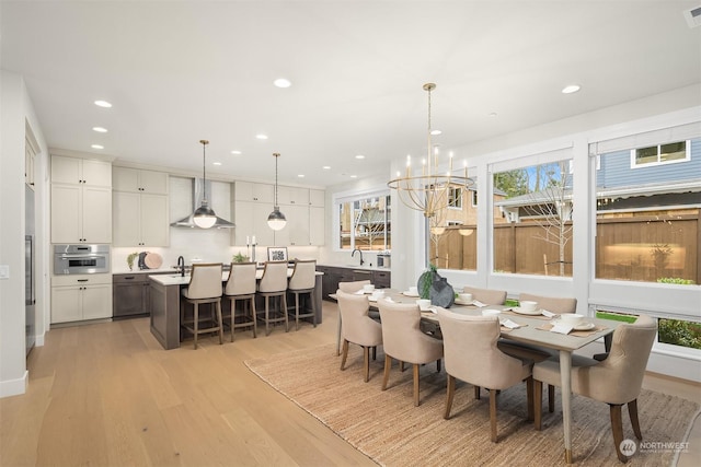 dining space with sink, light wood-type flooring, and a notable chandelier