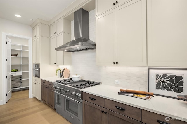 kitchen with stainless steel appliances, light wood-type flooring, dark brown cabinets, and wall chimney exhaust hood