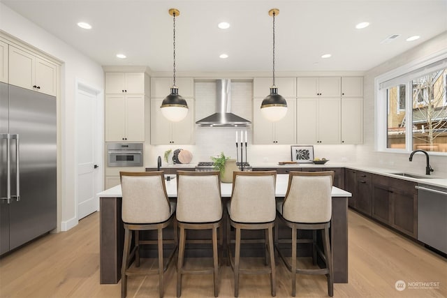 kitchen featuring appliances with stainless steel finishes, pendant lighting, a kitchen island, wall chimney exhaust hood, and sink