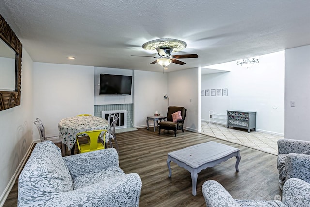 living room with wood-type flooring, a fireplace, ceiling fan, and a textured ceiling