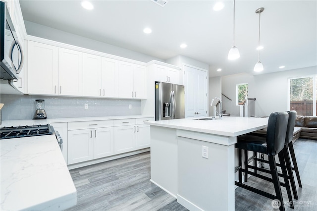 kitchen with a sink, backsplash, recessed lighting, stainless steel appliances, and light wood-style floors