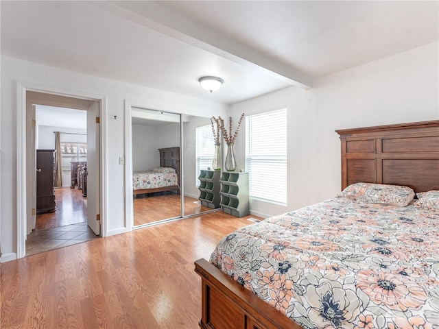 bedroom with light hardwood / wood-style floors, a closet, and beam ceiling