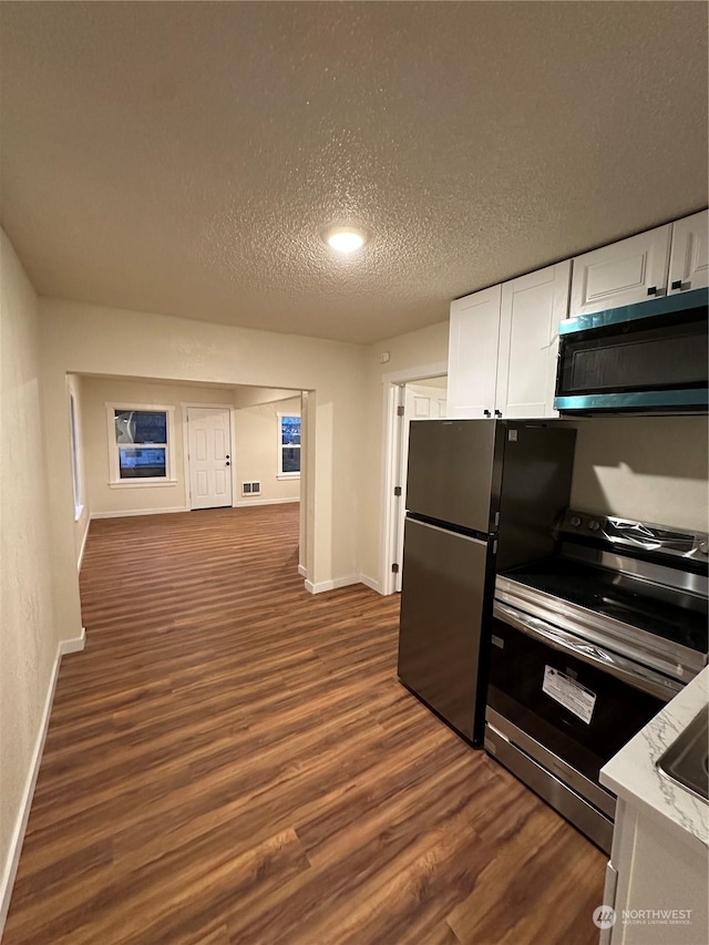 kitchen with a textured ceiling, stainless steel appliances, dark hardwood / wood-style floors, and white cabinets