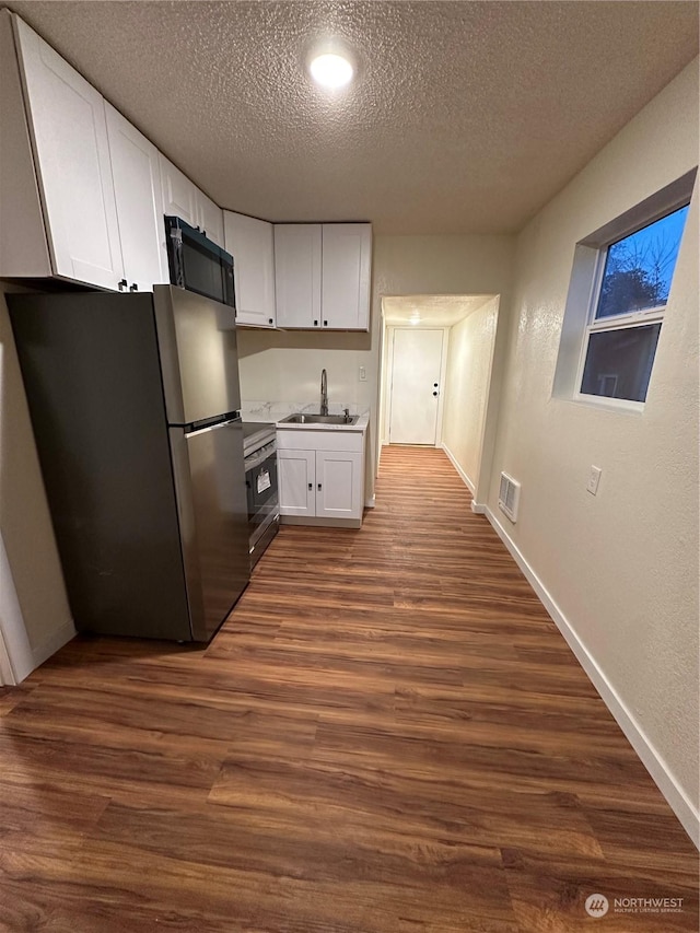 kitchen with appliances with stainless steel finishes, dark hardwood / wood-style floors, sink, and white cabinets