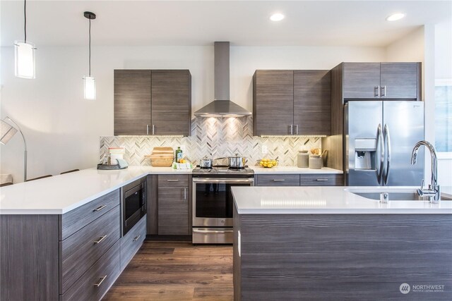 kitchen featuring pendant lighting, wall chimney exhaust hood, dark wood-type flooring, stainless steel appliances, and decorative backsplash