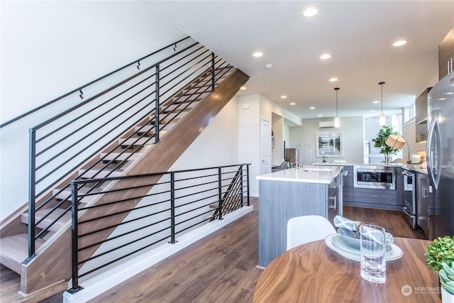 kitchen featuring dark wood-type flooring, a kitchen island with sink, appliances with stainless steel finishes, and pendant lighting