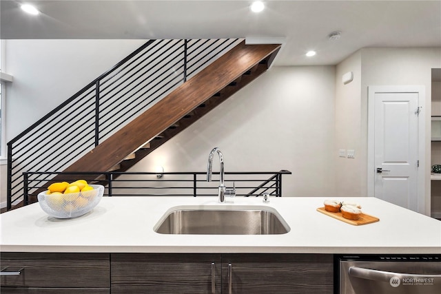 kitchen with dark brown cabinets, stainless steel dishwasher, a center island with sink, and sink