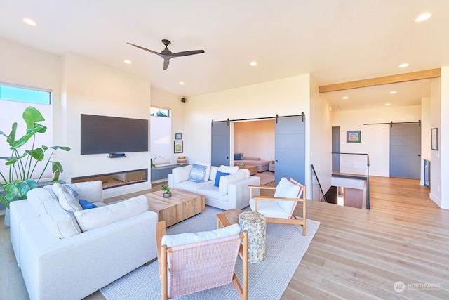 living room with ceiling fan, a barn door, and light hardwood / wood-style flooring