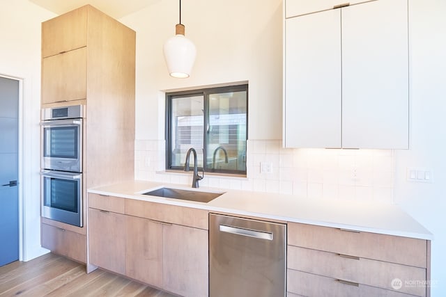 kitchen with appliances with stainless steel finishes, decorative backsplash, decorative light fixtures, light hardwood / wood-style flooring, and sink