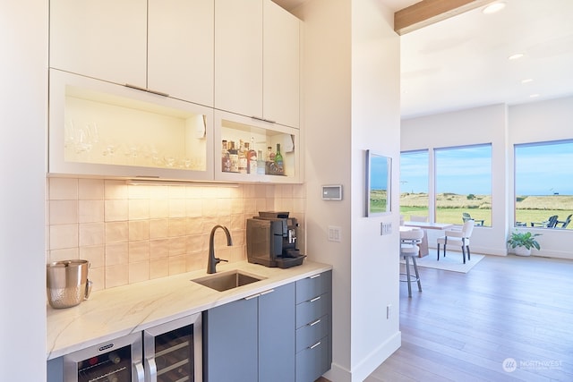 bar featuring tasteful backsplash, sink, light hardwood / wood-style flooring, light stone countertops, and beverage cooler