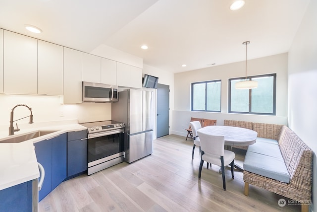 kitchen featuring white cabinetry, light hardwood / wood-style floors, appliances with stainless steel finishes, hanging light fixtures, and sink