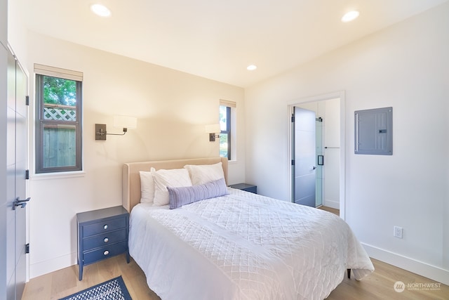 bedroom with vaulted ceiling, ensuite bathroom, electric panel, and light hardwood / wood-style flooring