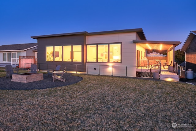 back house at dusk featuring a wooden deck and a yard