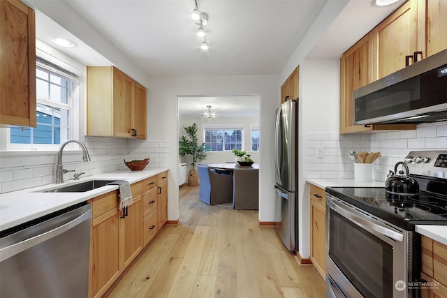 kitchen with light hardwood / wood-style flooring, decorative backsplash, an inviting chandelier, appliances with stainless steel finishes, and sink